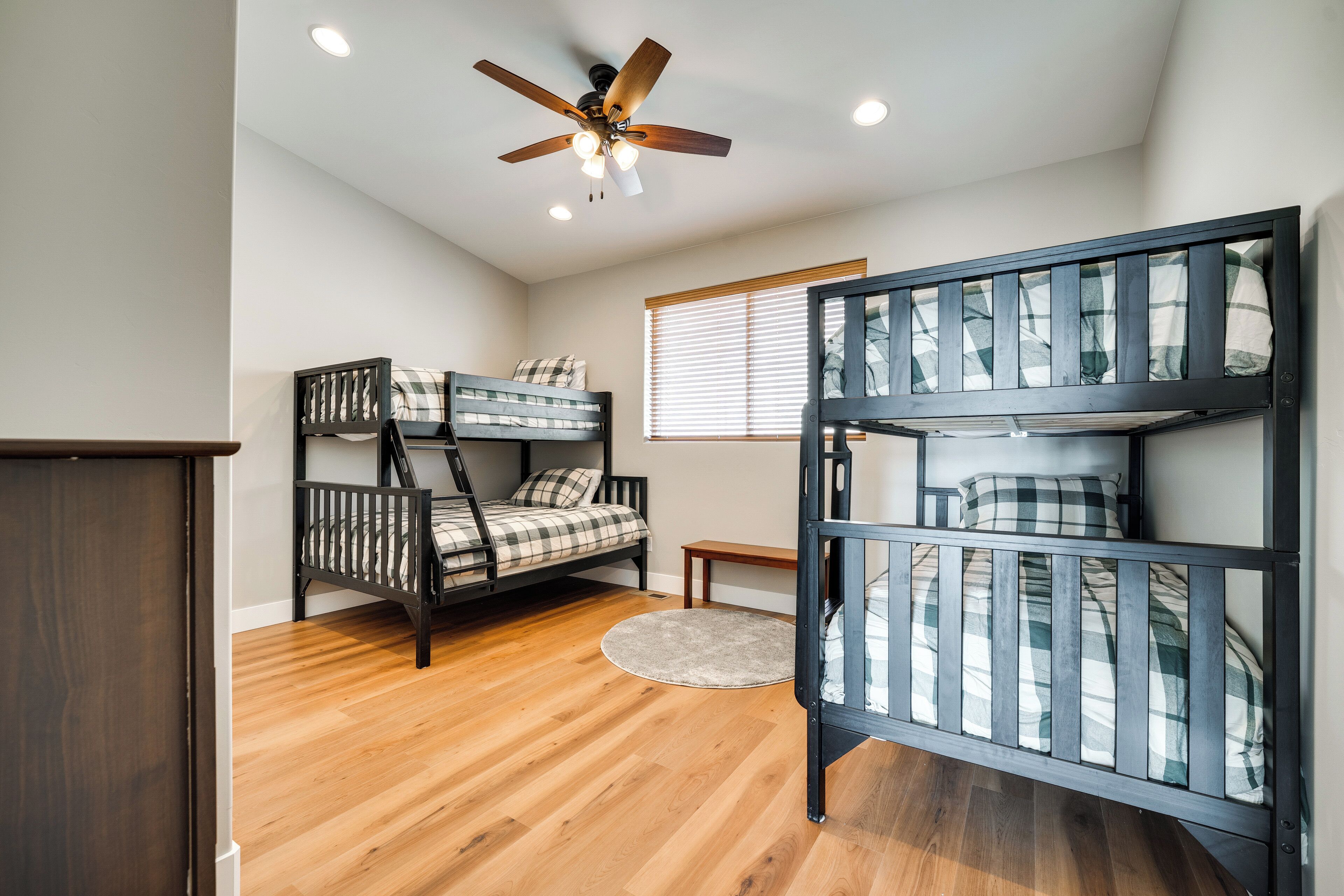 A bedroom with two bunk beds, a ceiling fan, a window with blinds, and a wooden floor.