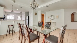 A dining area with a glass table, wooden chairs, a chandelier, and a kitchen in the background. - 4 Mi to Dtwn Brownsville: Family Home w/ Yard! (Brownsville)