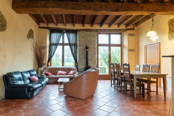 A living room with a sofa, a chair, a dining table with chairs, a stone pillar, and large windows.