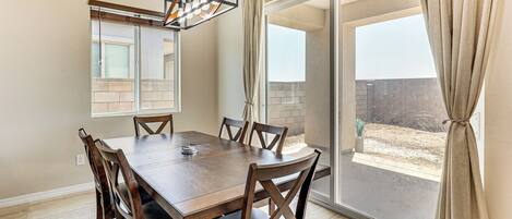 Zona pranzo con tavolo e sedie in legno, lampadario e vista su un patio esterno attraverso una porta in vetro.