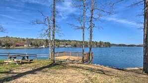 A lakeside park with a wooden deck, picnic tables, and a view of a lake with buildings in the background. - Walk to Lake Desoto: Home w/ Hot Tub Access! (Hot Springs Village)