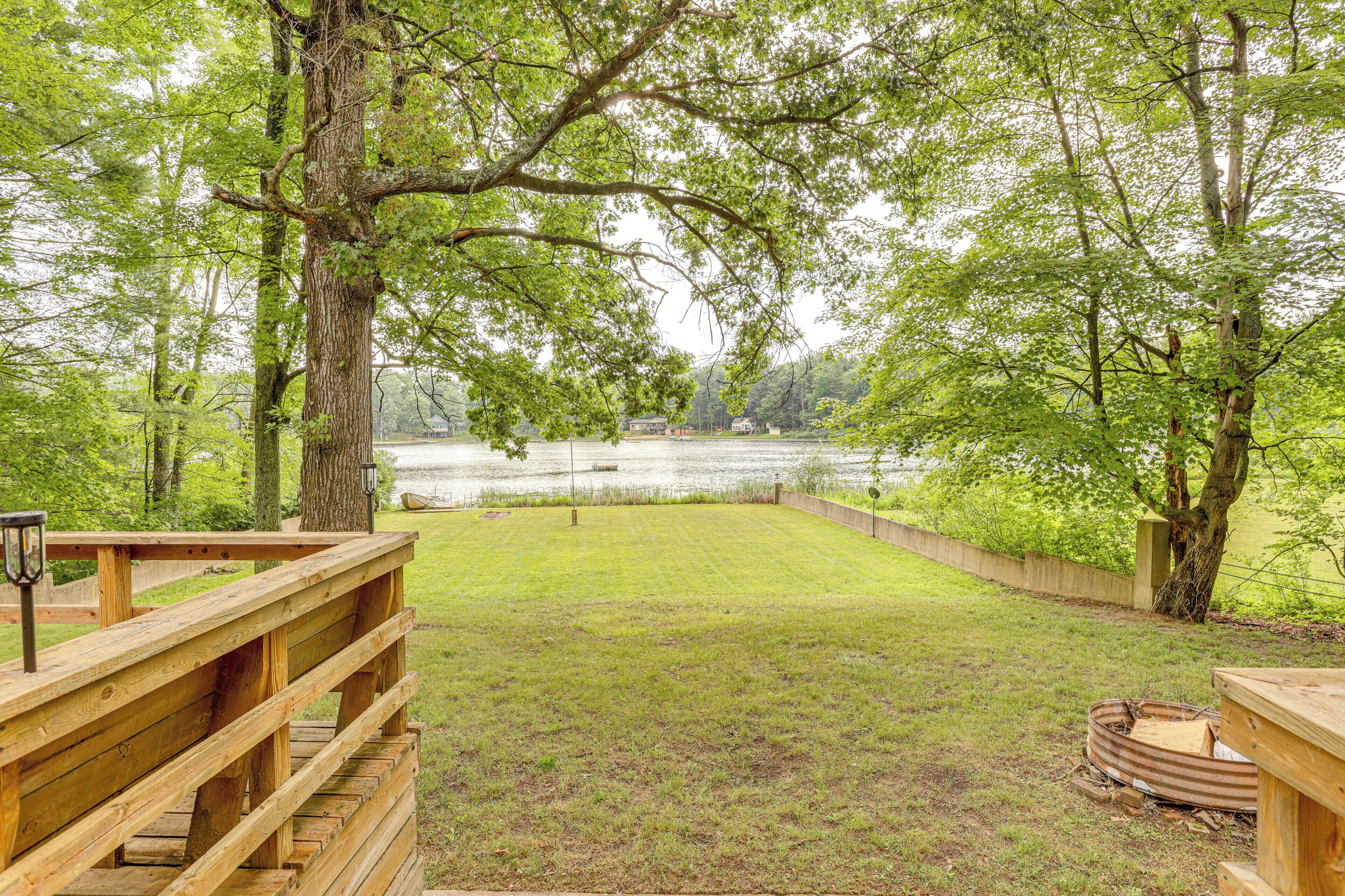 A wooden deck leading to a grassy area with a view of a lake and trees.