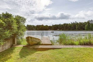 Ein Steg am See mit einem Boot, umgeben von Wiesen und Bäumen.