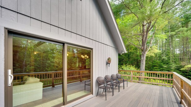A wooden deck with outdoor seating, a glass door leading to a covered area, and a view of a forested area. - White Mountain Retreat! 3 Mi to Cannon Mountain (Franconia)