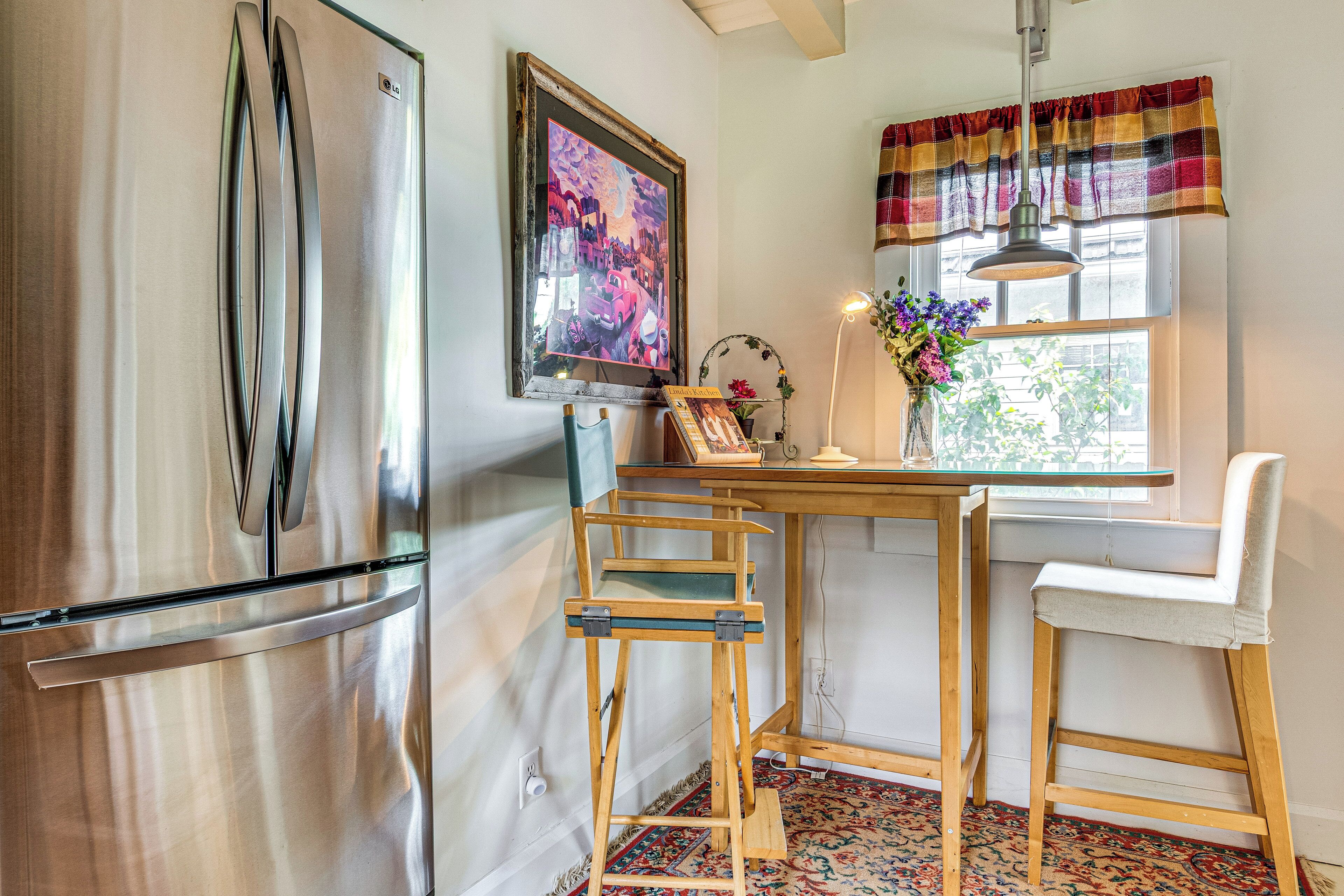 A kitchen with a stainless steel refrigerator, a wooden table, a chair, and a window with a curtain.
