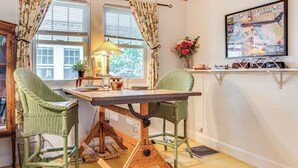 A dining area with a wooden table and two wicker chairs, a lamp, and a framed poster on the wall.