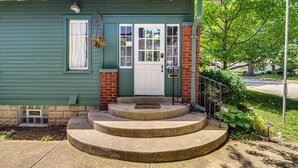 A two-story house with a green exterior, a white front door, and a small front porch with steps leading up to it.