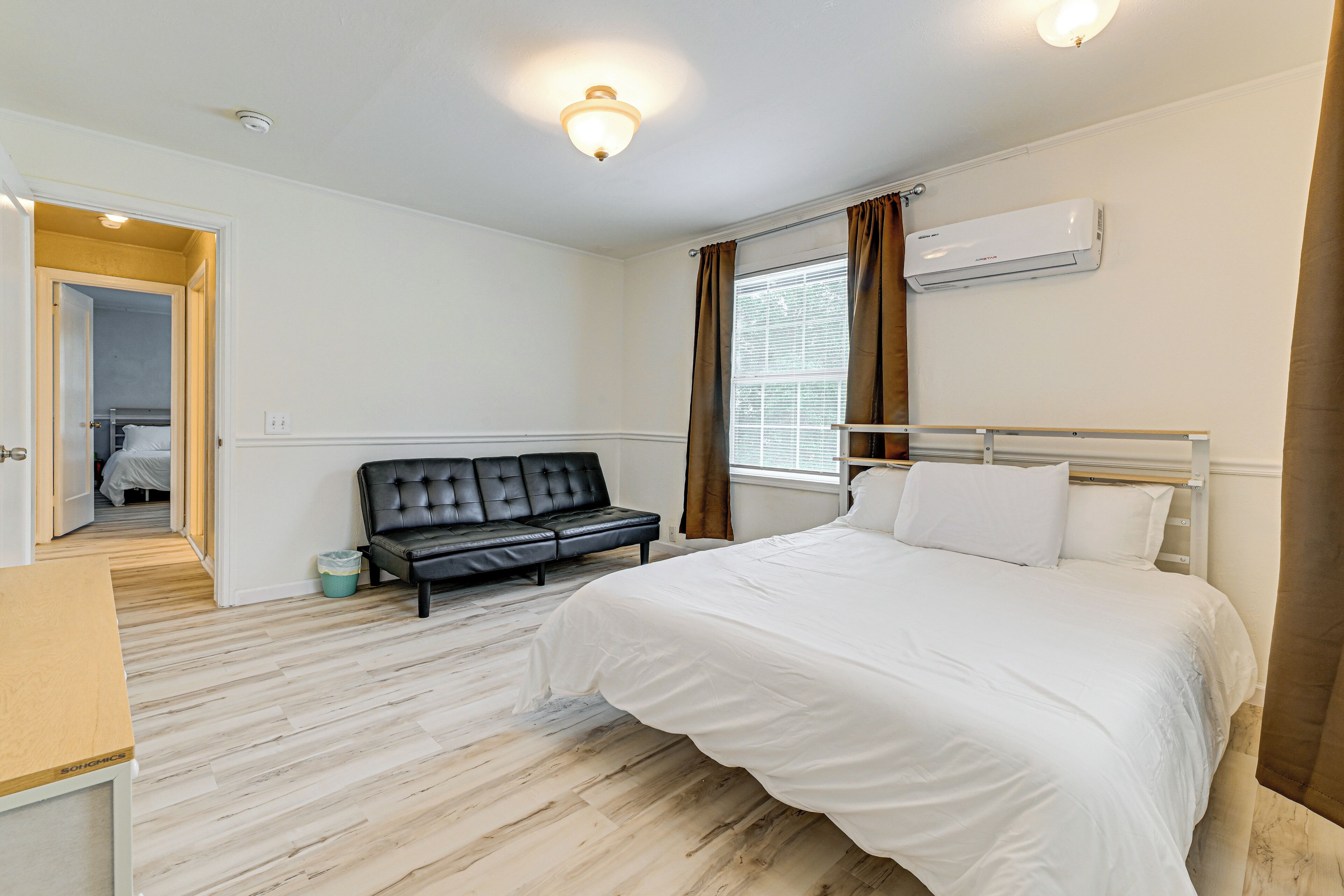 Un dormitorio con cama, sofá, aire acondicionado y ventana con cortinas.