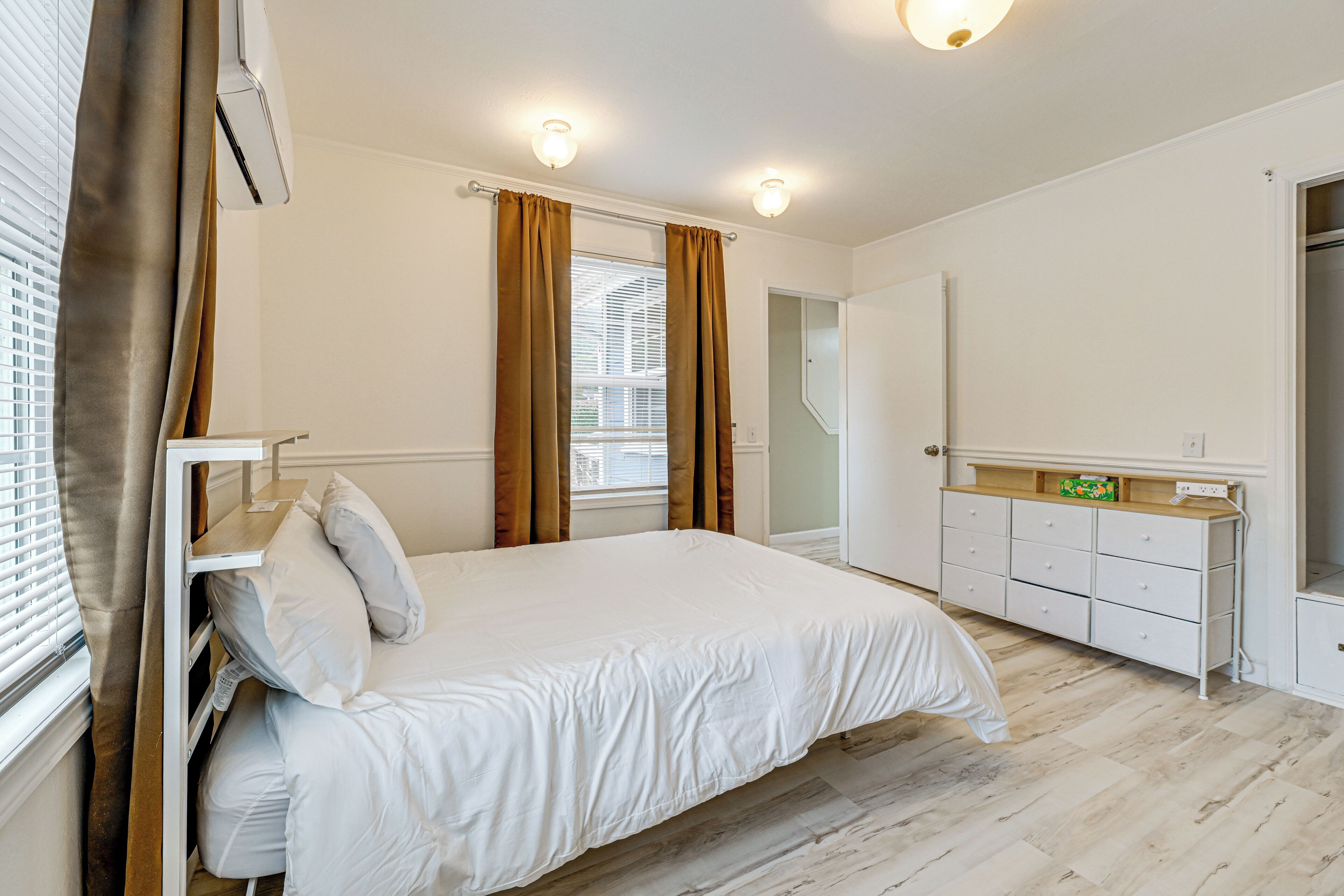 A bedroom with a bed, a dresser, a mirror, and a window with curtains.
