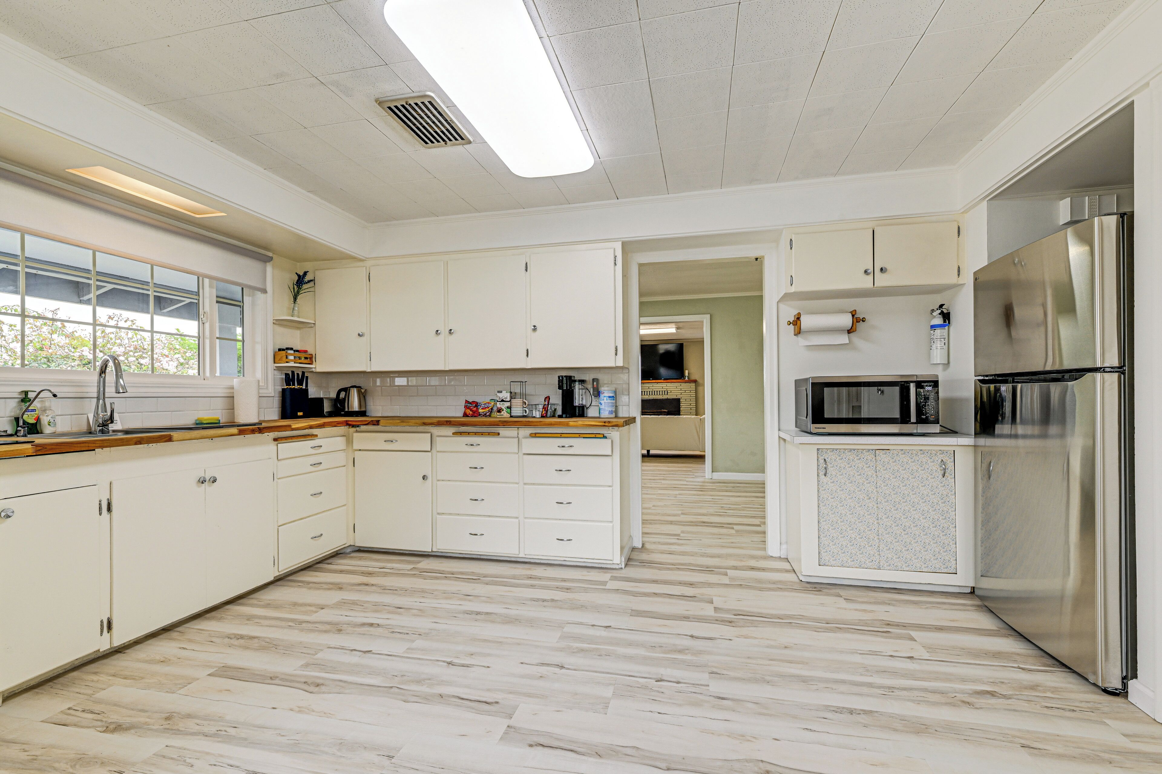 A modern kitchen with white cabinets, a stainless steel refrigerator, and a large window.