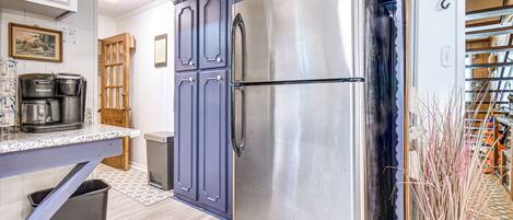 A kitchen with a stainless steel refrigerator, wooden cabinets, a coffee maker, and a trash bin.