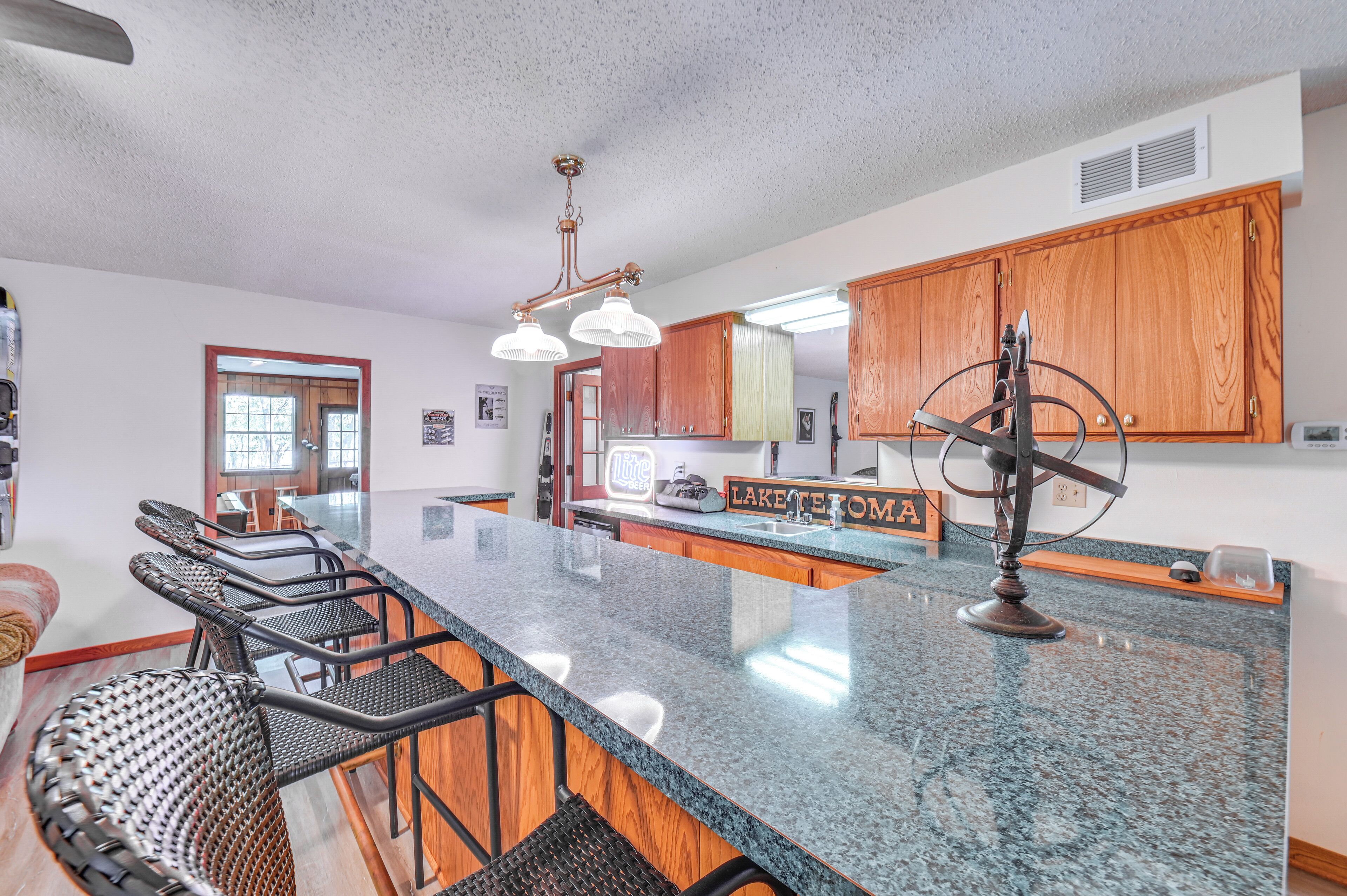 A kitchen with a granite countertop, wooden cabinets, and a bar area with wicker chairs.
