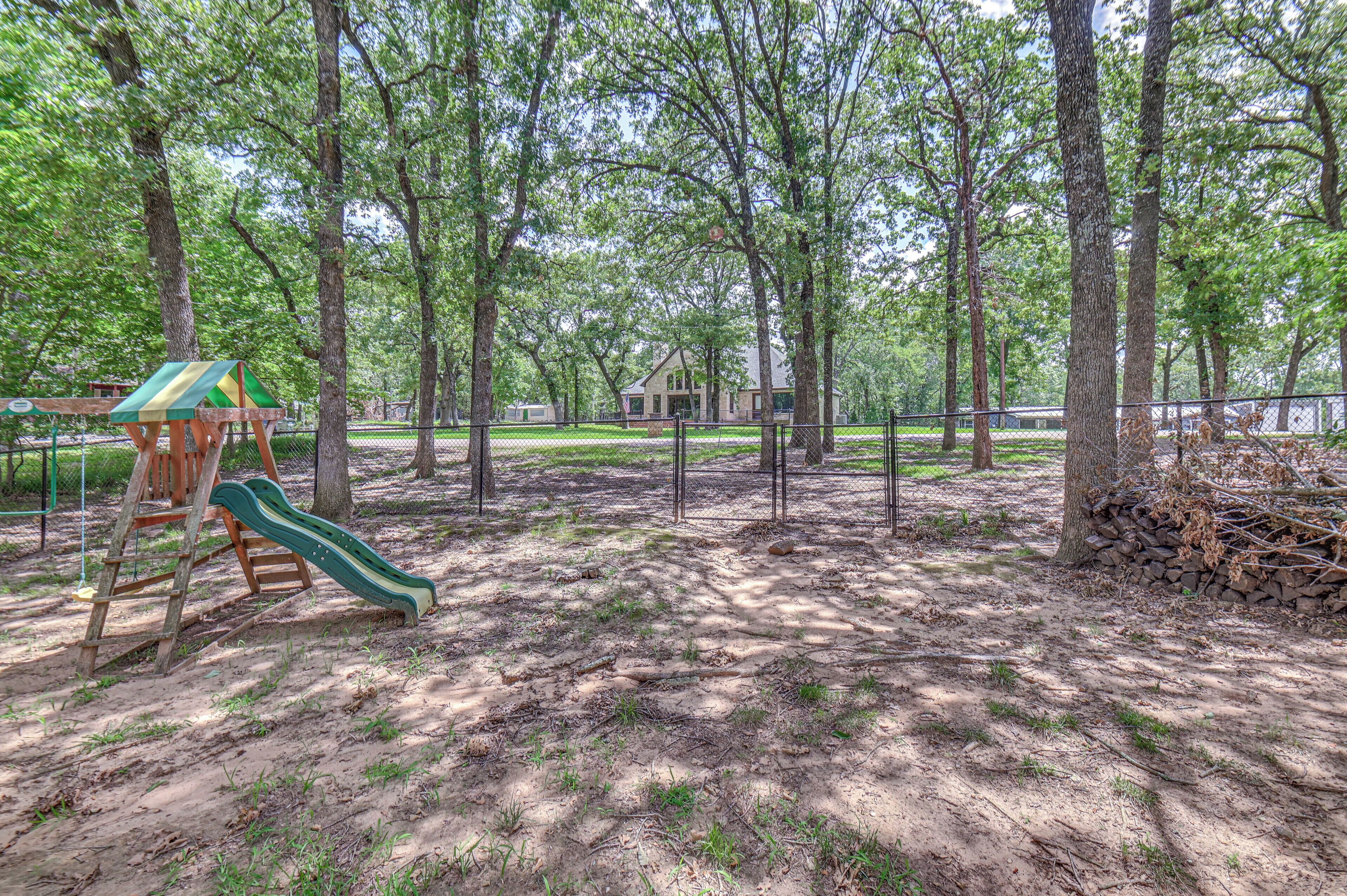 A playground with a slide and climbing structure, surrounded by trees and a house in the background.