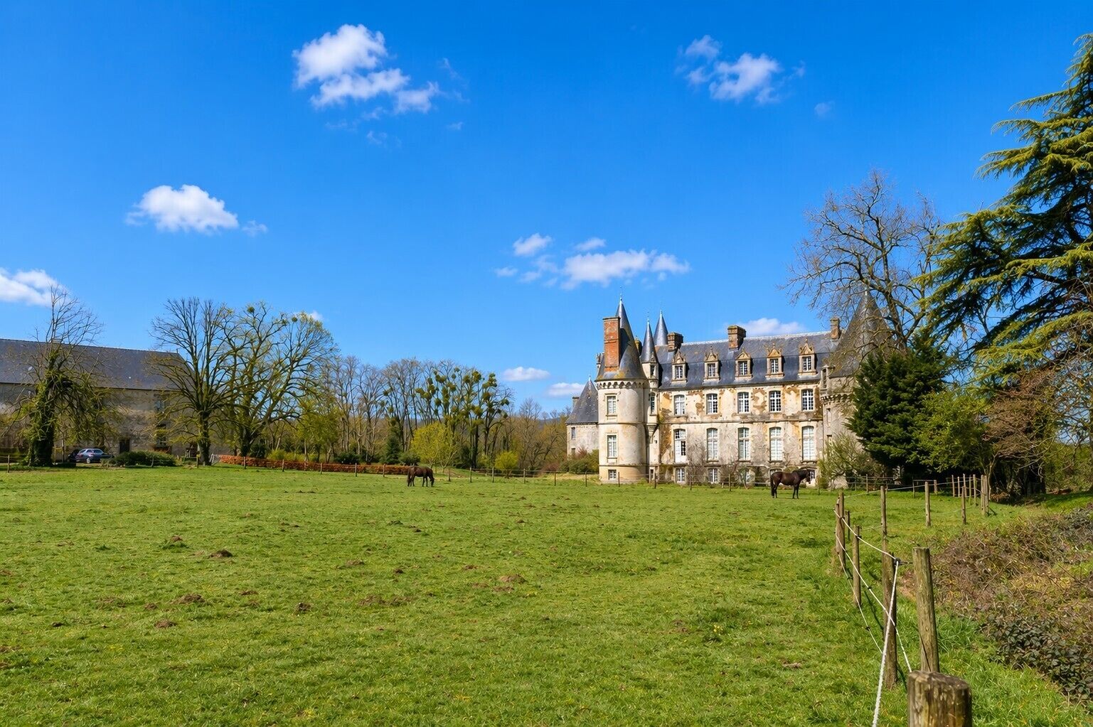 A large, historic building with a castle-like facade, surrounded by a grassy field and trees.
