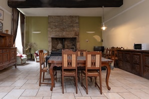 Un comedor con chimenea de piedra, sillas de madera, una mesa y un televisor sobre un mueble.