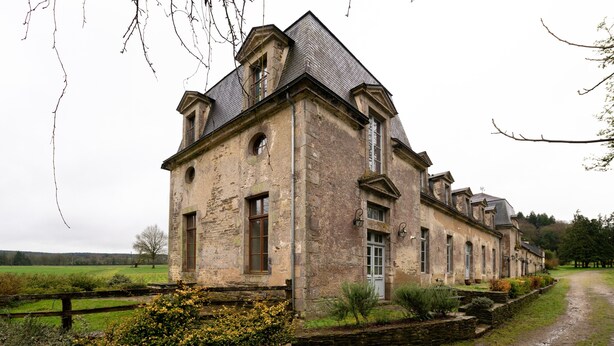 A stone building with a symmetrical facade, a central entrance, and a surrounding garden.