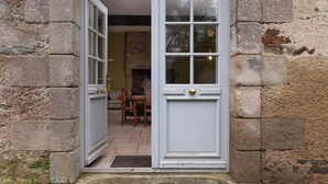 A stone building with a white door, a fireplace, and a dining area visible inside.