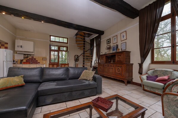 A living room with a black leather sofa, a wooden cabinet, and a staircase. - Holiday Home 'Le Crévy - Le Chateau - 8 Pers' with Private Terrace, Shared Garden and Wi-Fi (Val d'Oust)