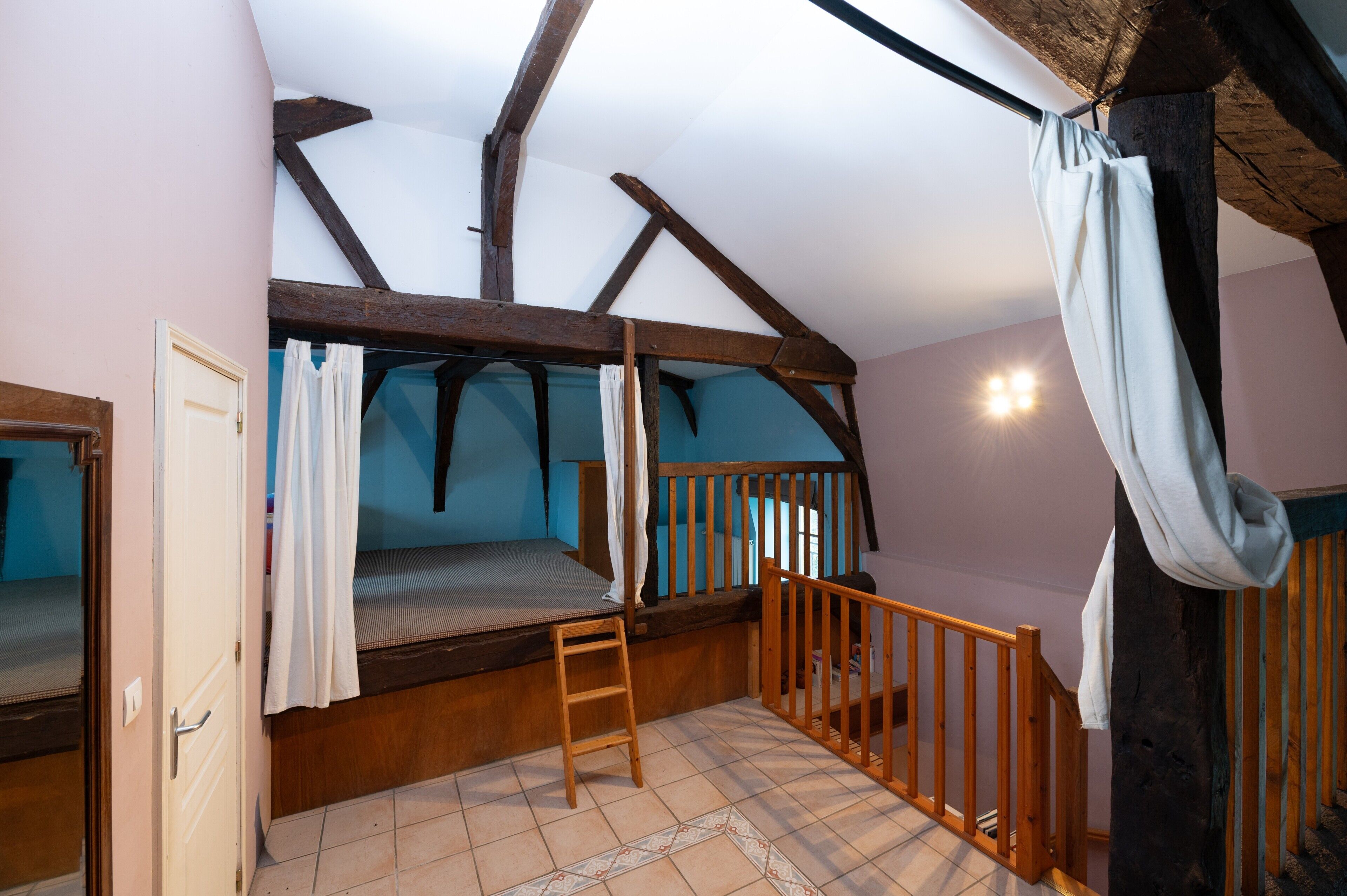 A dormitory-style room with bunk beds, a wooden ladder, a small wooden staircase, and a door.
