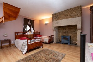 A bedroom with two wooden beds, a stone fireplace, and a small wood stove. - Holiday Home 'Le Crévy - Le Chateau - 8 Pers' with Private Terrace, Shared Garden and Wi-Fi (Val d'Oust)