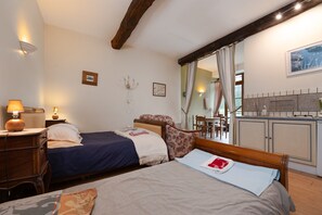 A bedroom with two beds, a wooden headboard, a nightstand, a lamp, and a view of the kitchen area.