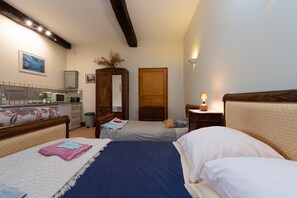 Une chambre avec deux lits, une armoire en bois, un miroir, une petite table avec une lampe et un coin cuisine.