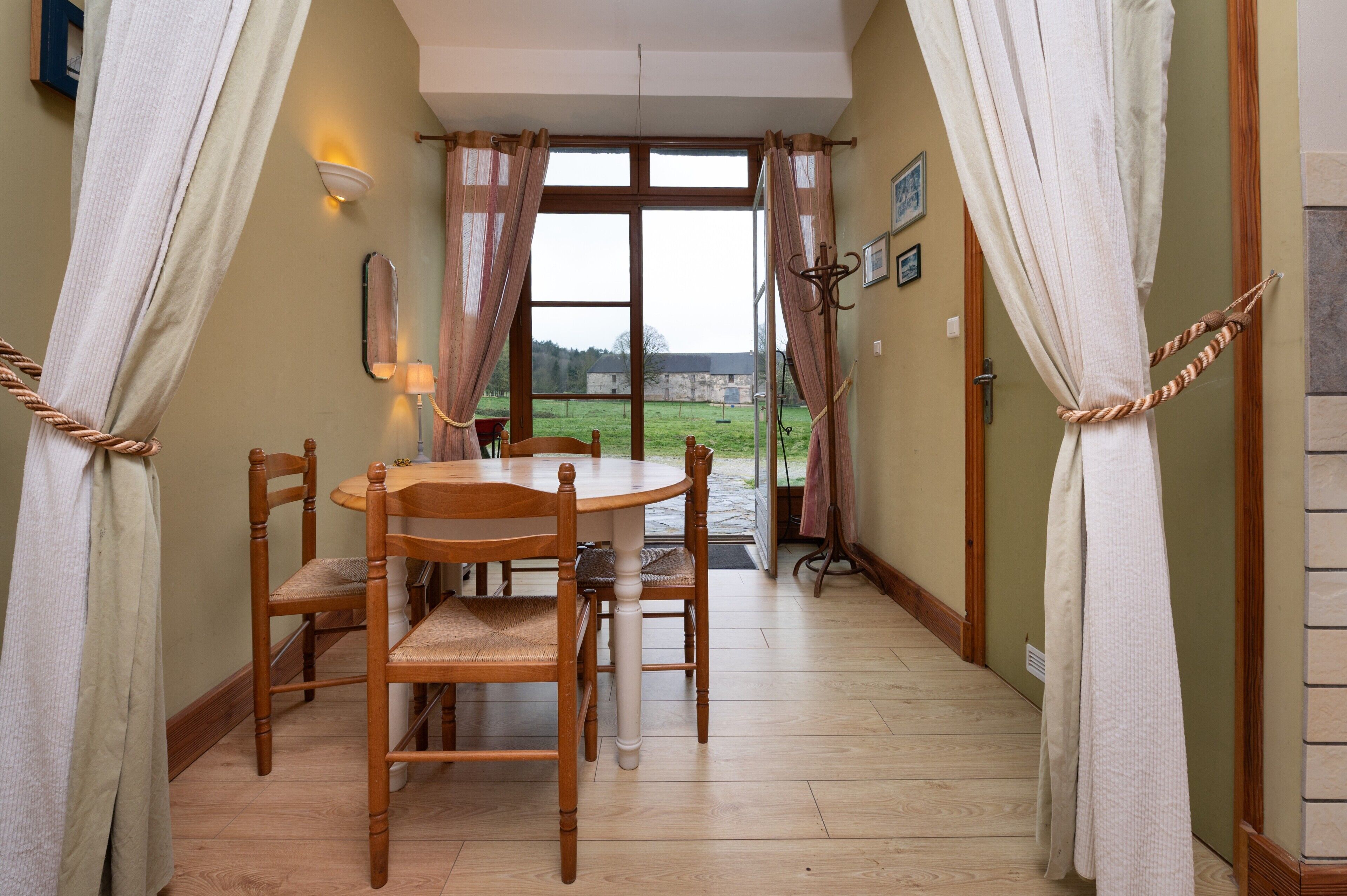 A dining area with a wooden table and chairs, a view through a glass door, and curtains tied back.