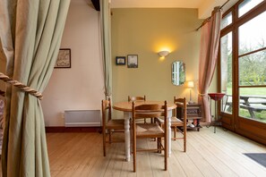 Un coin repas avec une table ronde en bois et des chaises, un miroir au mur et une fenêtre avec des rideaux.