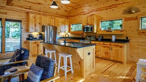 Una cabaña de madera con cocina que cuenta con una isla central, taburetes de bar y ventanas amplias.