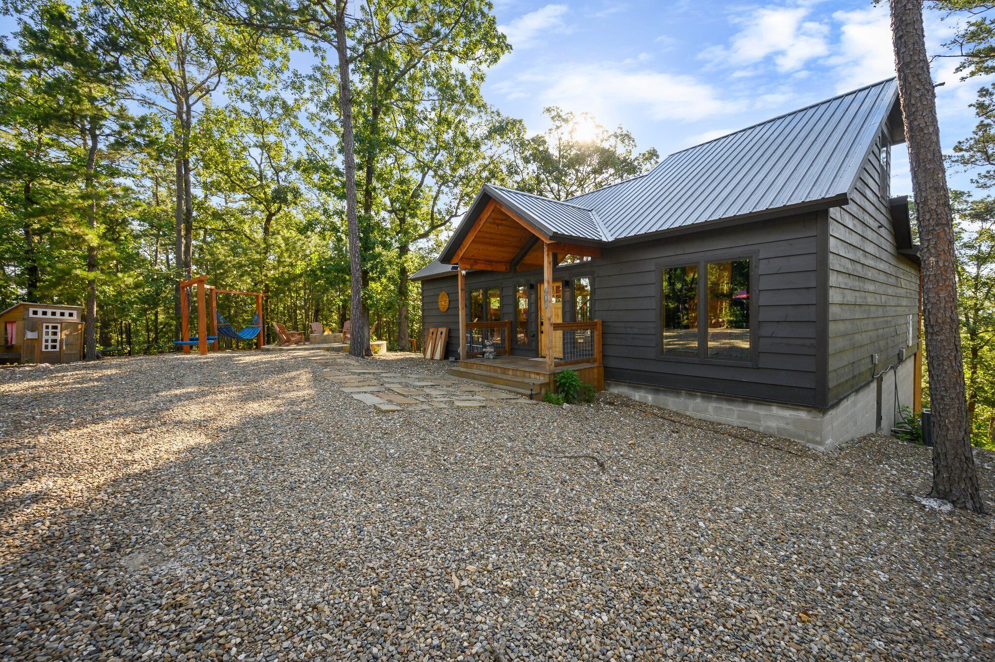 Een chalet met een grindpad, houten terras en een metalen dak.