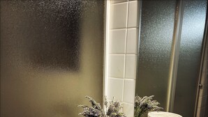 Ein Badezimmer mit einem weißen Waschbecken, einem Spiegel, einer weißen Vase mit Blumen, einer Glasdose und einem Korb.