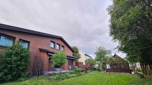 Een woonwijk met een bakstenen huis, een klein houten gebouw en een verzorgd gazon.