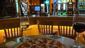 A bar area with a pizza on a table, two glasses of wine, and a television screen in the background.