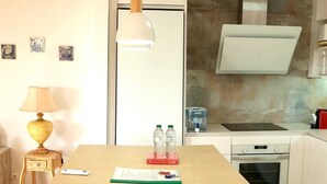 A modern kitchen with a central island, bar stools, a pendant light, and a small dining table with a lamp.