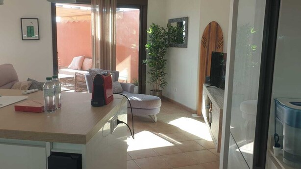 A living room with a sofa, a table with items, a TV, and a view of the outside.