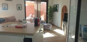 Ein Wohnzimmer mit einer Couch, einem Tisch mit Gegenständen, einem Fernseher und Blick ins Freie.