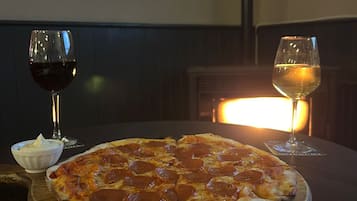 Una pizza sobre una tabla de madera, en una mesa redonda, con dos vasos de vino.