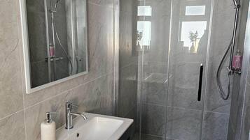 A modern bathroom with a large mirror, a sink with a soap dispenser, a shower with a handheld showerhead, and a glass-enclosed shower stall.