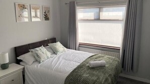 A neatly made bed with a green blanket, a bedside table with a lamp, and a window with curtains. - Cortoon Inn, Double Room 7 (1 DBL) (Tuam)