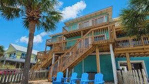 A multi-story wooden building with a balcony, a staircase, and several blue chairs in front.