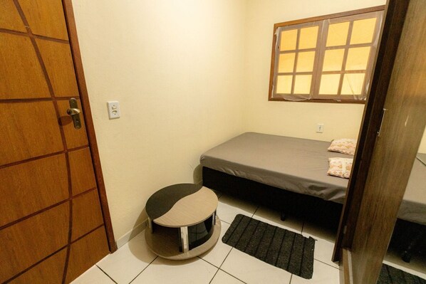 Una habitación pequeña y acogedora con una cama individual, un asiento redondo para gato y una ventana con persianas.