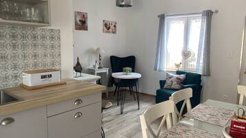 A kitchen with a bread box, a dining table with chairs, a blue sofa, and a window with curtains.
