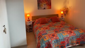 A bedroom with a wooden headboard, two bedside tables with lamps, a colorful quilt, and a painting on the wall.