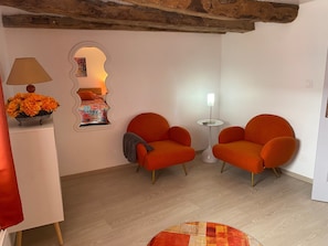A room with a bed, two orange armchairs, a small table with a lamp, a mirror, and a flower arrangement. - Holiday Home 'La Petite Cocotte' with Private Terrace, Private Garden and Wi-Fi (Marcheseuil)