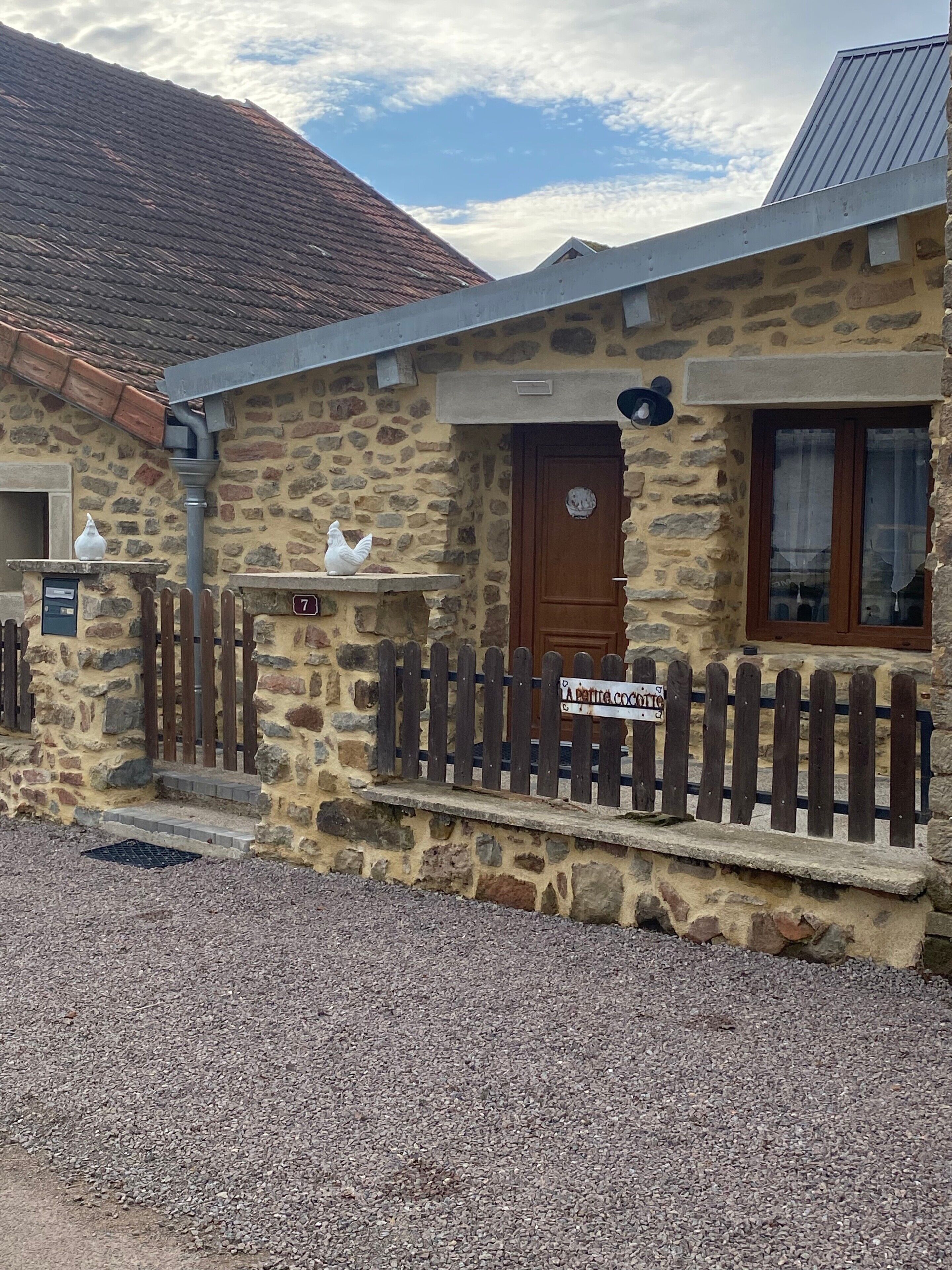 A stone building with a wooden door, a small porch, and a sign that reads 'A petite cottage.'