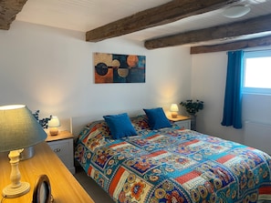 A bedroom with a colorful quilt, wooden headboard, bedside lamps, and a window with blue curtains. - Holiday Home 'La Petite Cocotte' with Private Terrace, Private Garden and Wi-Fi (Marcheseuil)