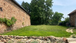A stone building with a grassy yard, potted plants, and a stone wall.