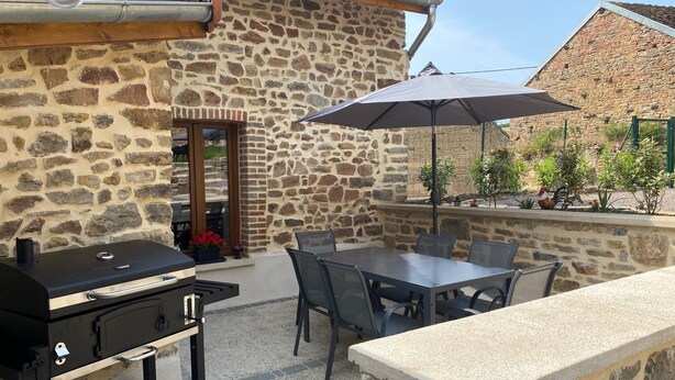 An outdoor patio with a stone wall, a grill, a table with chairs, and an umbrella.