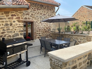 An outdoor patio with a stone wall, a grill, a table with chairs, and an umbrella. - Holiday Home 'La Petite Cocotte' with Private Terrace, Private Garden and Wi-Fi (Marcheseuil)