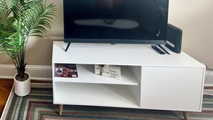 Un téléviseur à écran plat, posé sur un meuble blanc, avec une télécommande et un haut-parleur noir.
